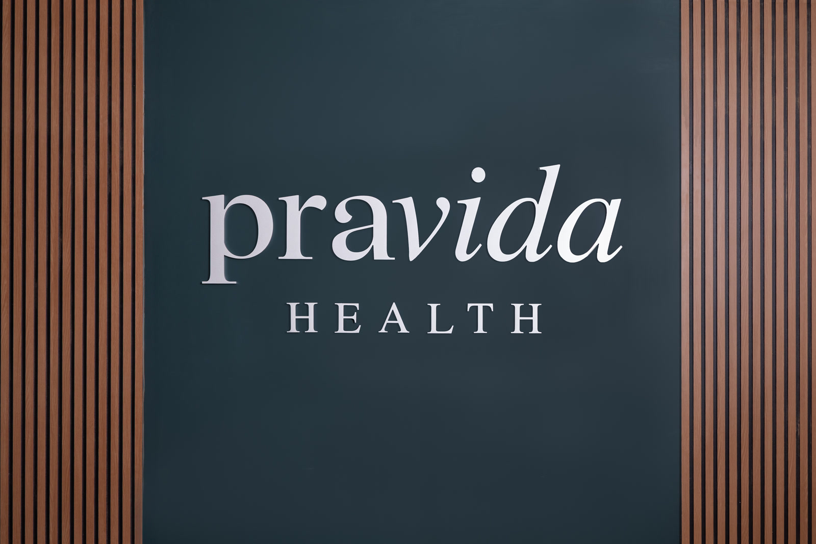 Pravida Health logo on signature teal wall with wood slat accents